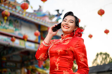 Asian beautiful woman wearing a cheongsam use mobile phone at shrine