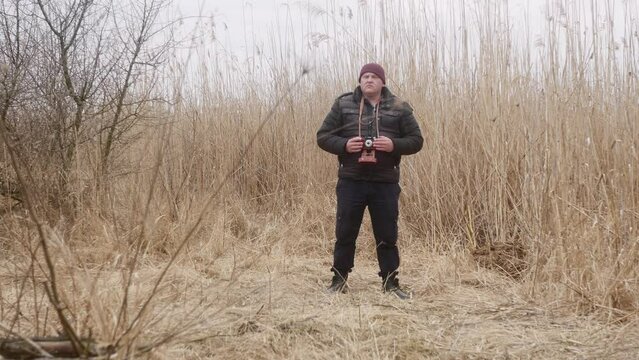 a man in nature takes pictures on a vintage film camera against the background of early spring lake reeds