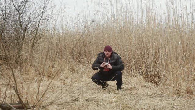 a man squatting takes pictures on a vintage film camera against the background of early spring lake reeds