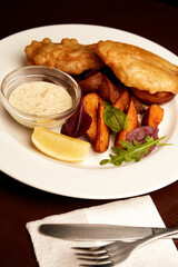 battered fish on a plate with chips on a wooden table in pub. unhealthy food