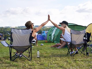 Tuinposter Happy campers. Rearview shot of two friends giving each other a high five at an outdoor festival. © Julie Francoeur/peopleimages.com