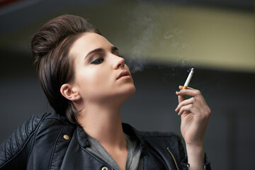 Obraz premium Attitude and attractive. Shot of a rebellious looking young woman smoking a cigarette in a car garage.