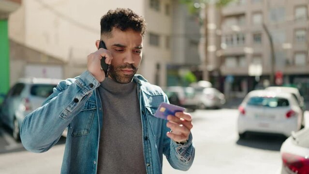 Young arab man talking on the smartphone and using credit card at street