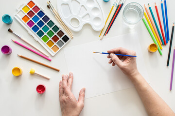 The female hands while drawing. View from above. artist's desk with colorful paints and pencils....