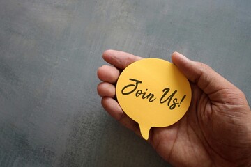 Hand holding yellow speech bubble with text JOIN US! with copy space. Registration and hiring.