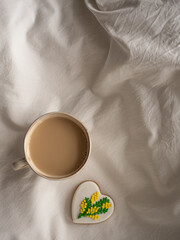 Morning coffee with milk with heart-shaped cookies painted with mimosa pattern icing  on a white bed in the morning light