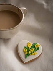 Morning coffee with milk with heart-shaped cookies painted with mimosa pattern icing  on a white bed in the morning light