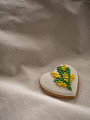 Heart-shaped cookies painted with mimosa pattern icing on a white bed in the morning light