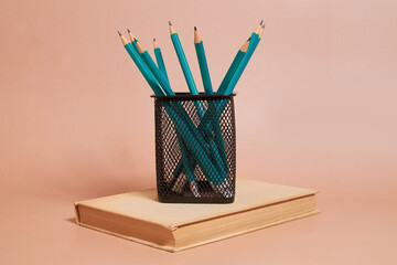 A glass with graphite pencils stands on an old book on a colored background