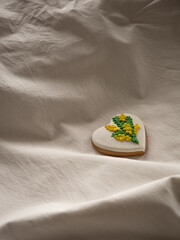 Heart-shaped cookies painted with mimosa pattern icing on a white bed in the morning light