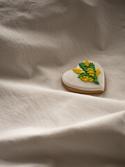 Heart-shaped cookies painted with mimosa pattern icing on a white bed in the morning light