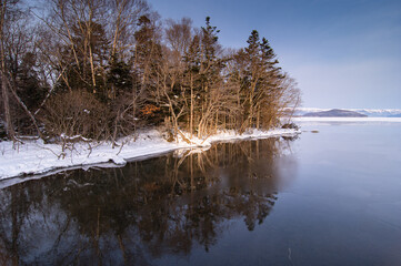 湖面に森の木々を映す冬の湖畔の風景。北海道の屈斜路湖。