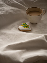 Morning coffee with milk with heart-shaped cookies painted with mimosa pattern icing  on a white bed in the morning light