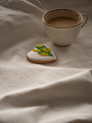 Morning coffee with milk with heart-shaped cookies painted with mimosa pattern icing  on a white bed in the morning light