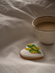 Morning coffee with milk with heart-shaped cookies painted with mimosa pattern icing  on a white bed in the morning light