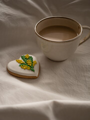 Morning coffee with milk with heart-shaped cookies painted with mimosa pattern icing  on a white bed in the morning light