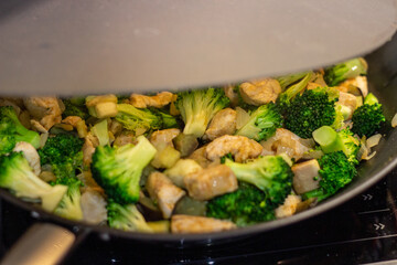 A delicious Chinese dish is fried chicken with broccoli in a wok. The process of cooking chicken with broccoli vegetables in a steel pan. Teriyaki chicken and broccoli in a cast-iron pan. 