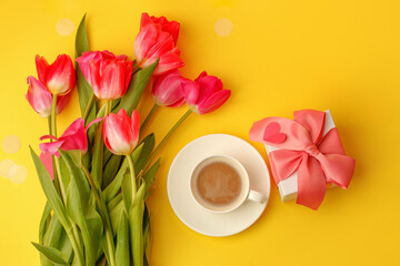 Beautiful spring breakfast on Mothers or Womans International day 8 march, 14 february. Bouquet of pink tulips, gift, coffee cup on bright yellow table. Flat lay, banner for site, seasonal flyer
