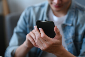 Cropped shot young man using smart phone for checking social media, ordering delivery at home.