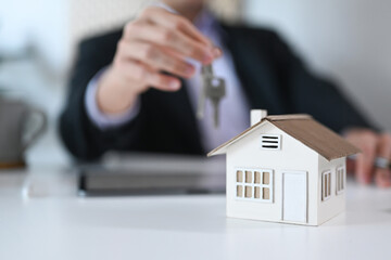 Close up view house model on white table and businessman holding keys in background. Real estate, moving home or renting property.