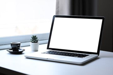 Laptop computer, cactus and coffee cup on white table in bright living room.