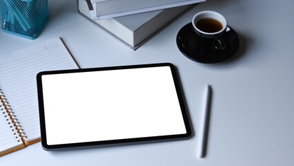 Digital tablet, stylus pen, coffee cup, and notebook on white office desk.