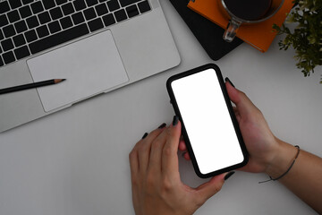 Above view young woman holding mockup mobile phone with empty screen on office desk.