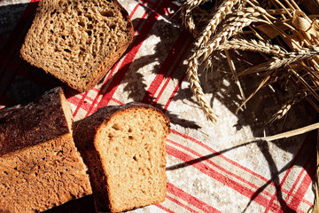 Sliced sourdough bread on on rustic red- gray kitchen towel and spikelets of wheat. Table top view, natural sun light