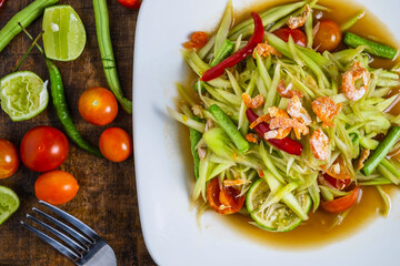 Thai food, papaya salad and tomatoes, peppers and condiments on a wooden table