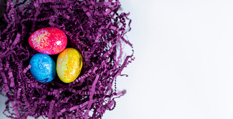 Happy Easter card. Easter eggs on the background of a purple nest, top view on a white background, image with selective focus. Copy space for text.