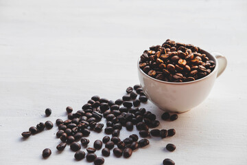 Roasted coffee beans in a coffee cup on a white table