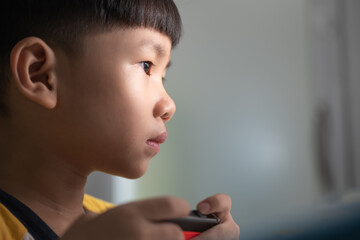 Asian boy about 5 years old using a wireless controller for playing a video game.