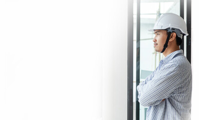 A young engineer, wearing a white hat, white shirt, standing with his arms crossed, looks out with determination. To work on the design of residential buildings. 