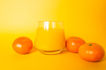 Glass of fresh orange juice with three citrus mandarin fruits near. Isolated on the yellow background.