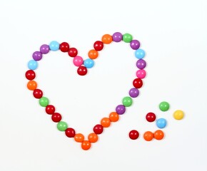Sweet heart made from colored smarties. Chocolate candies in a shape of heart on white background, flat lay.