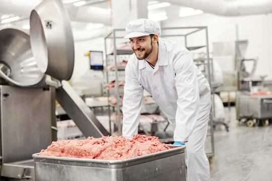 A meat factory worker pushing ground beef.
