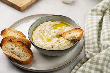 Traditional dish of arabic cuisine baba ganoush made of roasted eggplant, tahin, cilantro, garlic, olive oil, lemon juice with toasted baguette croutons on grey background