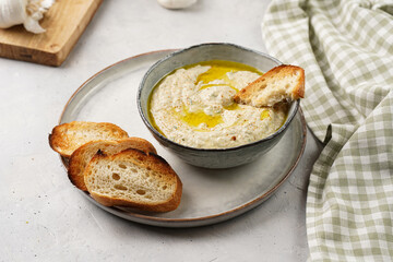 Traditional dish of arabic cuisine baba ganoush made of roasted eggplant, tahin, cilantro, garlic, olive oil, lemon juice with toasted baguette croutons on grey background