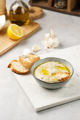 Traditional dish of arabic cuisine baba ganoush made of roasted eggplant, tahin, cilantro, garlic, olive oil, lemon juice with toasted baguette croutons on grey background, white marble board