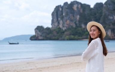 Portrait image of a beautiful young asian woman close her eyes while strolling on the beach with the sea and blue sky background