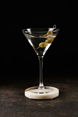 Transparent non-alcoholic beverage with olives and thyme on wooden board on black background and bar equipment