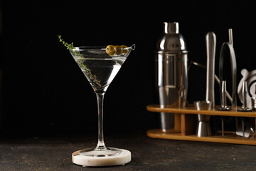 Transparent non-alcoholic beverage with olives and thyme on wooden board on black background and bar equipment