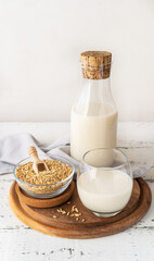 Oat milk in glass and bottle with whole grain oats