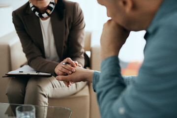 Close up of supportive mental health professional holding hands with her patient during the therapy.