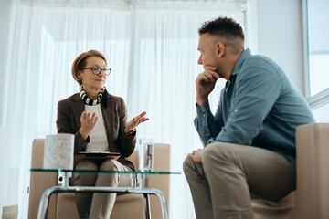 Mature psychotherapist talks to her patient during counseling session in her office.