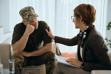 Depressed veteran listens to his supportive counselor during therapy session at mental health...