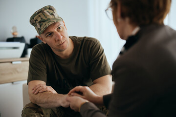 Sad military man talks to mental health professional while holding hands with her during counseling.