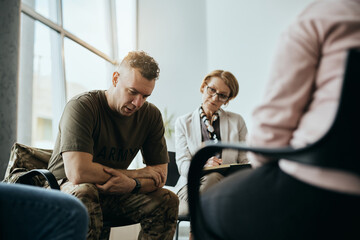 Depressed military man talks during group therapy meeting at mental health center. - obrazy, fototapety, plakaty