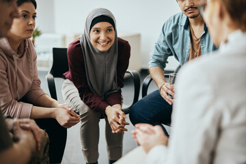 Happy Muslim woman and attenders of group therapy talk with their psychotherapist during meeting at communicatee center. - obrazy, fototapety, plakaty