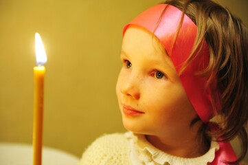 Little girl on Easter with a candle in the church on the child's glove a pink ribbon and a candle...